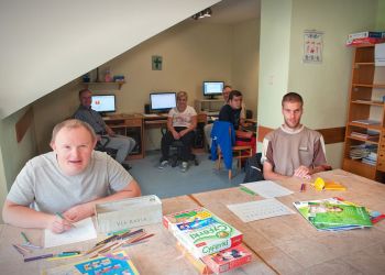 Powiększ zdjęcie: podopieczni w pracowni komputerowej, na pierwszym planie 2 podopiecznych przy stole, w tle podopieczni siedzą przy komputerach