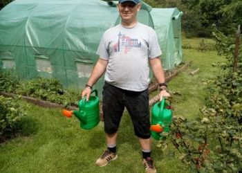 Powiększ zdjęcie: podopieczny w ogrodzie trzyma konewki do podlewania kwiatów, w tle foliak i grządki