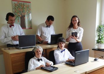 Powiększ zdjęcie: podopieczni z terapeutką podczas zajęć w pracowni komputerowej