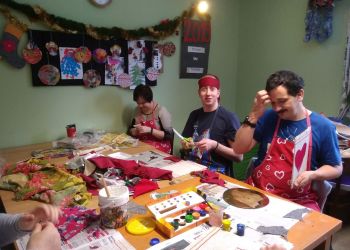 Powiększ zdjęcie: podopieczni przy stole podczas zajęć wycinają i wyklejają