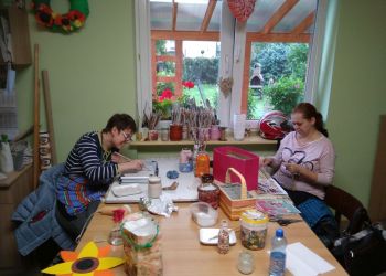 Powiększ zdjęcie: podopieczne przy stole malują i wykonują prace ręczne