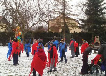 Powiększ zdjęcie: podopieczni w niebieskich i czerwonych płachtach chodzą z Marzanną zimą w ogrodzie