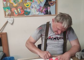 Powiększ zdjęcie: mężczyzna przy stole koloruje obrazek czerwoną kredką