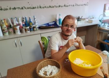 Powiększ zdjęcie: mężczyzna siedzi przy stole i targa papier do żółtej miski