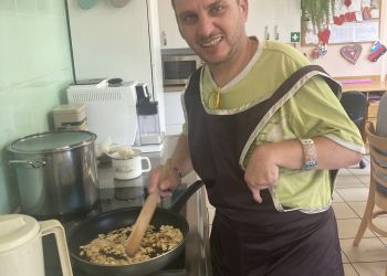 Powiększ zdjęcie: mężczyzna stoi przy kuchence i miesza łyżką potrawę na patelni