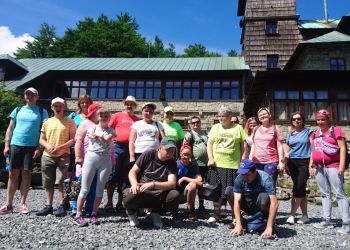 Powiększ zdjęcie: grupa osiemnastu osób w kolorowych koszulkach i spodenkach stoi przed schroniskiem górskim na Szyndzielni