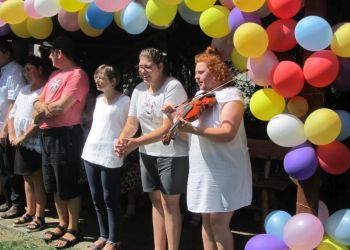 Powiększ zdjęcie: sześć osób stoi pod kolorowymi balonami, kobieta na pierwszym planie w rudych włosach gra na skrzypcach