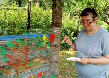 Powiększ zdjęcie: kobieta w szarej bluzce w ogrodzie maluje kolorowy obraz na folii