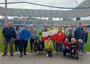 Powiększ zdjęcie: grupa piętnastu osób stoi na tle murawy stadionu miejskiego w Bielsku-Białej, jedna osoba w środku trzyma flagę biało-czerwoną