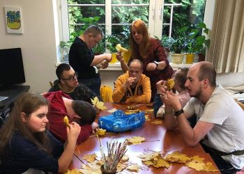 Powiększ zdjęcie: grupa podopiecznych przy stole wykonuje bukiety z żółtych liści klonu